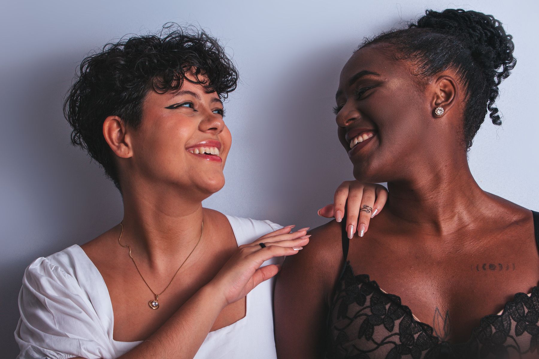 Two women smiling at each other in a studio portrait.
